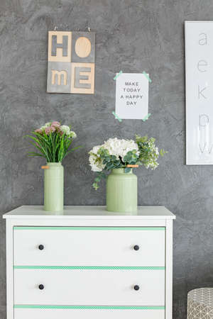 White chest of drawers and vaces with flowers against grey wallの写真素材