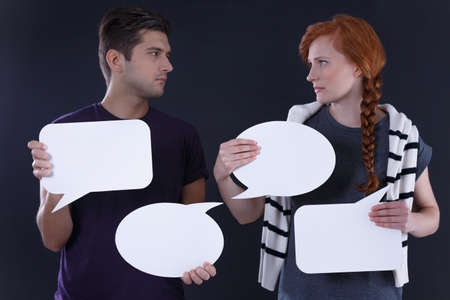 Young couple holding blank speech bubbles, dark backgroundの写真素材