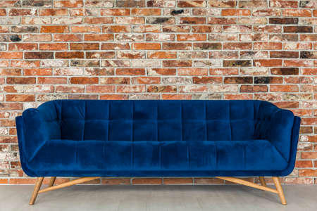 Red brick wall and vintage upholstered blue sofa