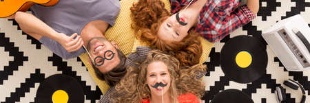 Friends posing with funny paper party attributes like glasses and moustachesの写真素材