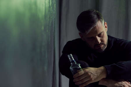 Alcohol addicted man sitting alone with alcohol bottleの写真素材