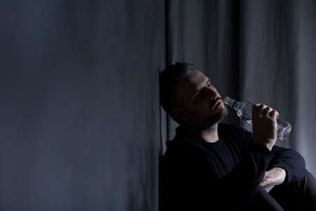 Drank man sitting alone with bottle of alcoholの写真素材