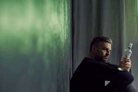 Broken man sitting with bottle of alcoholの写真素材