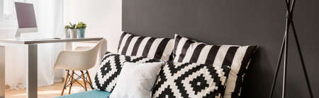 Closer shot of bedhead with pillows and home working area at the background