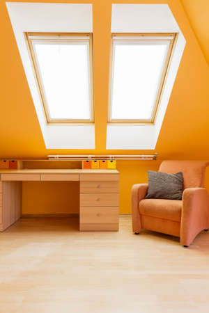Bright attic room in warm colours with desk, armchair and roof windowの写真素材