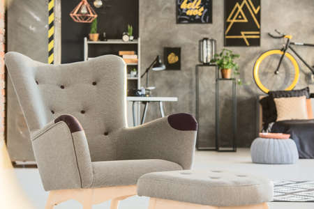 Grey room with stylish upholstered chair and pouf