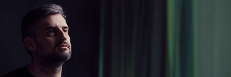 Sad, handsome widower standing in dark room, panorama
