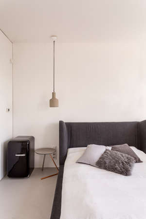 White bedroom with dark grey bed and compact fridge