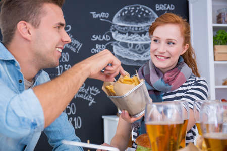 Smiled girl is sharing junk food with her friend