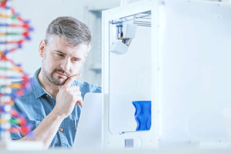 Pensive man working at laboratory, using 3d printer