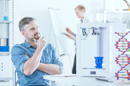 Man with 3D printer sitting at light officeの写真素材