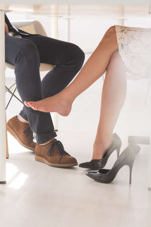 Closeup shot of a woman seductively touching a man's calf with her leg under the tableの写真素材
