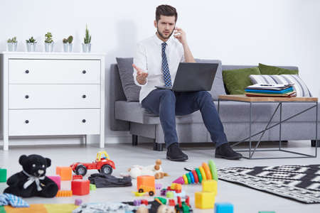 Busy single father talking on phone, child's toys on floor