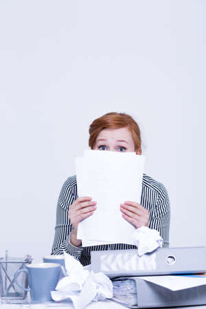 Frightened and insecure woman is hiding behind papersの写真素材