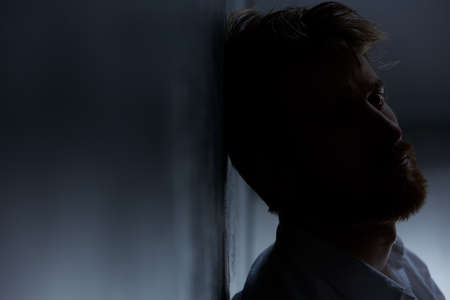 Young man suffering from depression, sitting alone in dark roomの写真素材