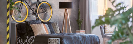 King-size bed in dark hipster bedroom with a bicycle on a wallの写真素材