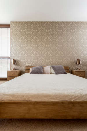 Queen size wooden bed with pillows in modern brown bedroom interiorの写真素材