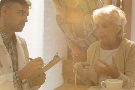 Worried doctor talking with elderly patient during home visit