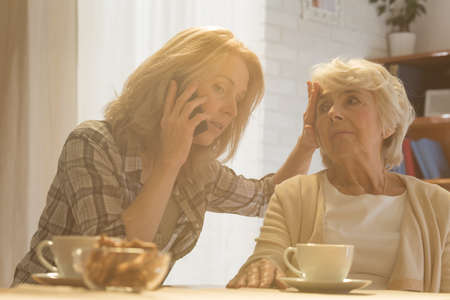 Worried female caregiver calling the doctor to her senior patient