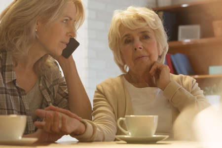Adult woman checking her older mother's pulse and calling the doctorの写真素材