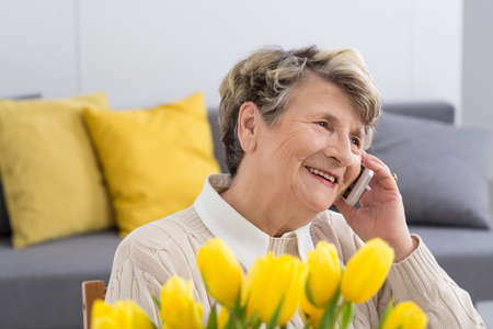 Happy senior woman talking on the phone in the living roomの写真素材