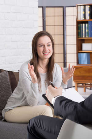 Smiling young woman visiting her psychologist and answering his questionsの写真素材