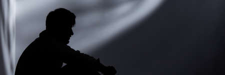 Lonely young man with fear of society sitting in the darknessの写真素材