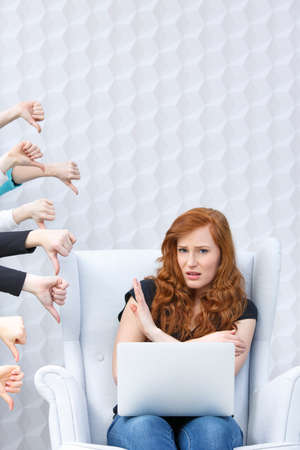 Disgusted girl with laptop and people hands with thumbs down