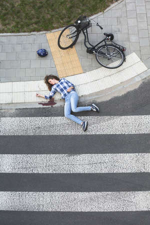 Bleeding car crash victim, lying unconscious on the pedestrian crossing next to her bikeの写真素材