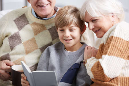Happy, small boy reading book with his grandparents