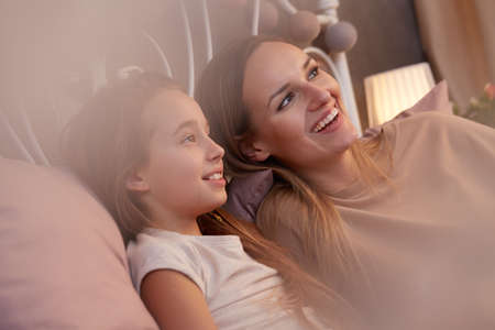 Happy mother and her daughter talking in the evening in bedの写真素材