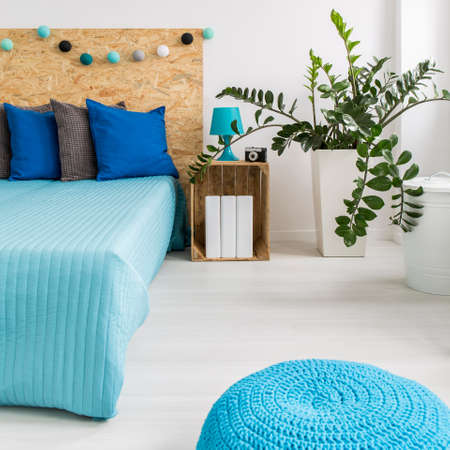 Light bedroom with double bed, plant and blue pouffeの写真素材