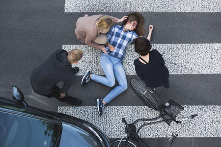 Passersby helping an unconscious casualty of a car accident lying next to the bikeの写真素材