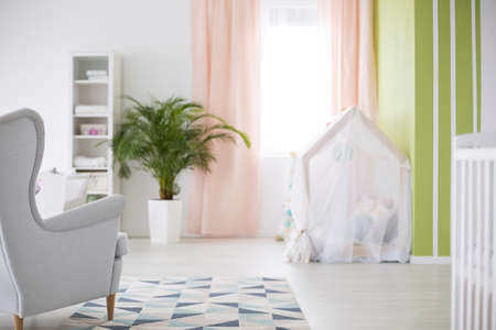 Spacious white baby room with armchair, plant and cribの写真素材