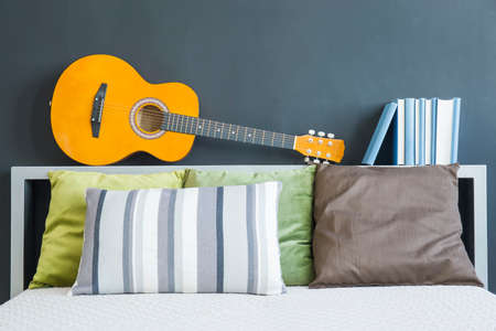 King-size bed with colorful pillows, guitar and booksの写真素材
