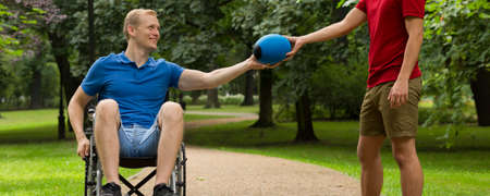 Cheerful man on a wheelchair taking the rugby ball from his friend