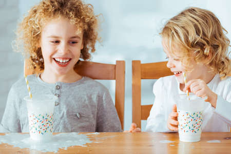 Happy siblings sitting beside table and drinking milkの写真素材