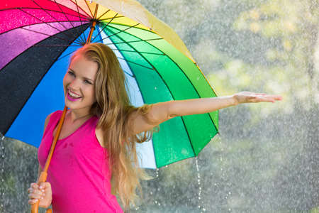 Happy woman holding colorful umbrella during summer rain