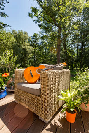 Guitar lying on a rattan garden sofa during sunny summer day