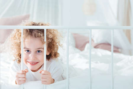 Cute, curly, blonde boy lying in bedの写真素材