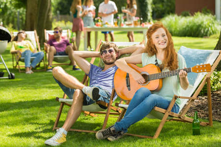 Woman sitting on sun bed, playing guitar in gardenの写真素材