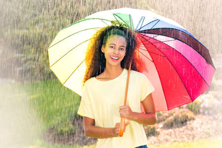 Beautiful afroamerican woman with umbrella standing in the rainの写真素材