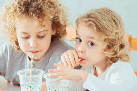 Cute, small siblings drinking healthy milk, sitting beside tableの写真素材