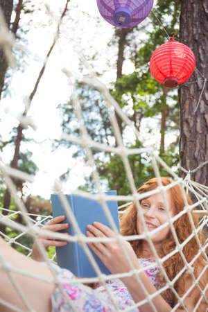 Shot of a smiling young woman reading a book while laying on a hammockの写真素材
