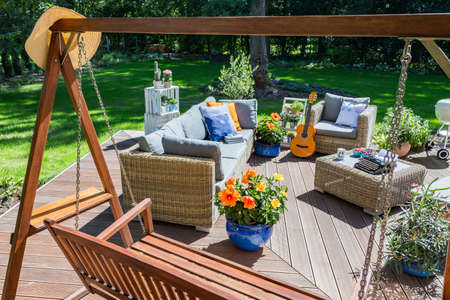 Spacious villa patio with garden swing, rattan firniture set, grill and guitar during summerの写真素材