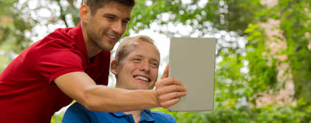Young man taking selfie of him and his disabled friend on wheelchairの写真素材