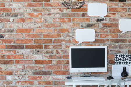 Computer on a desk against brick wall with empty mockup speech bubblesの写真素材