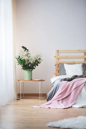 Modern bed and small nightstand with bunch of flowers in cozy bedroomの写真素材