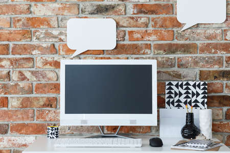 Modern desk with computer against brick wall with mockup speech bubblesの写真素材