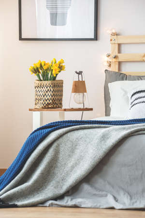 Grey bed and small nightstand with daffodils in modern bedroomの写真素材
